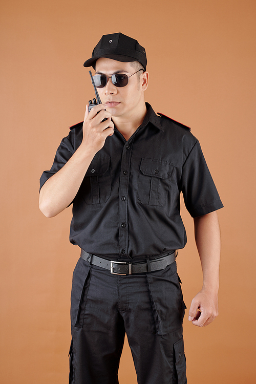 Police officer in black uniform, cap and sunglasses talking in walkie-talkie