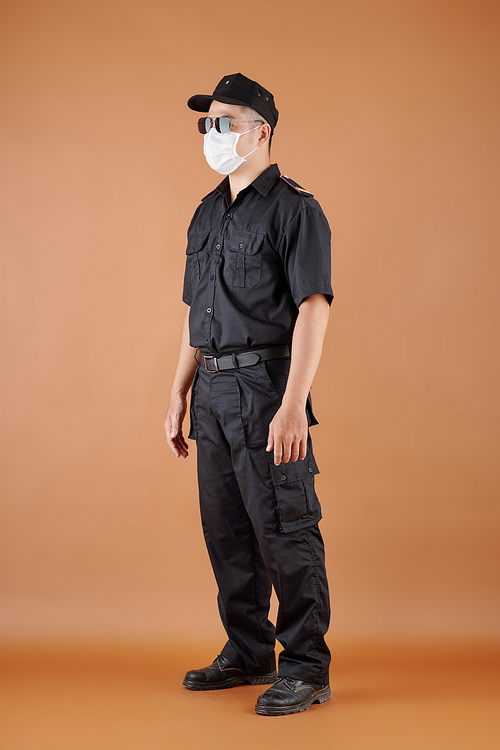 Full-length portrait of security guard in medical mask and sunglasses