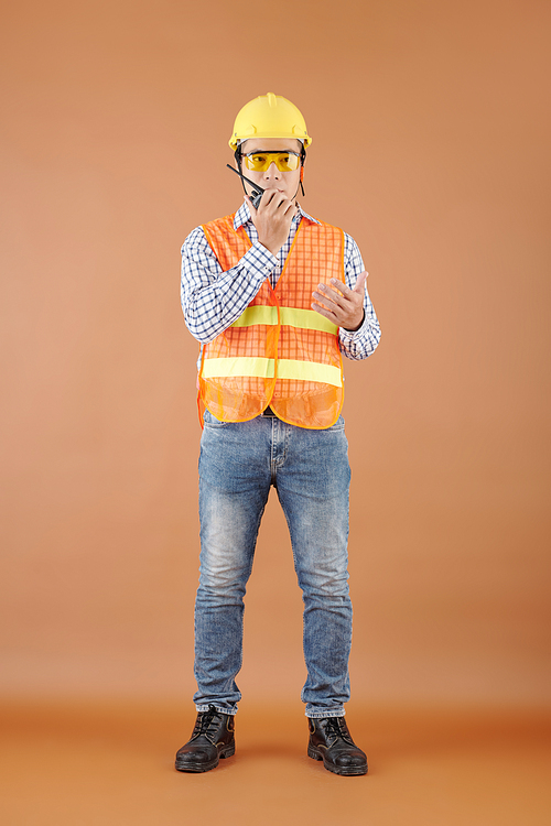 Portrait of contractor in orange vest, goggles and hardhat talking on walkie-talkie