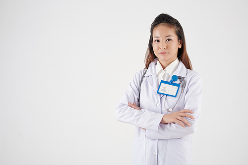Serious young Asian physician wearing labcoat when standing against white background