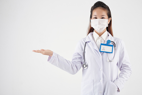 Young female doctor in protective mask and labcoat holding something in hand, isolated on white