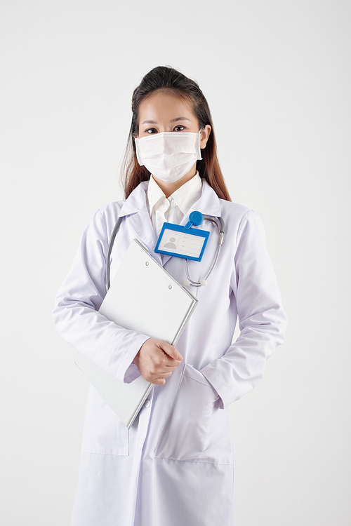Young general practitioner in protective mask holding documents folder and looking at camera