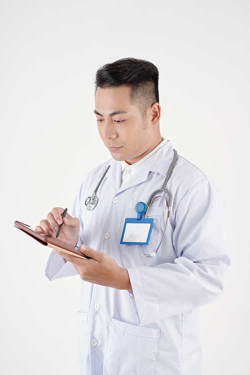 Serious physician checking medical card of patient on tablet computer and taking notes