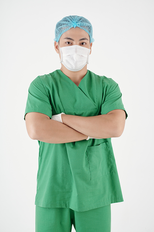 Portrait of serious surgeon in green scrubs and medical mask crossing arms and looking at camera