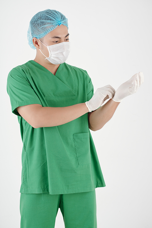 Serious surgeon in protective mask putting on rubber gloves before surgery