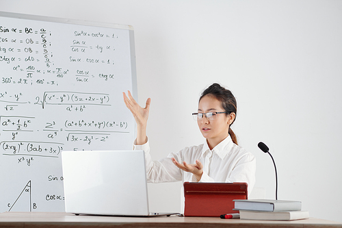 Young teacher with microphone on table explaining trigonometry formulas to students during online class