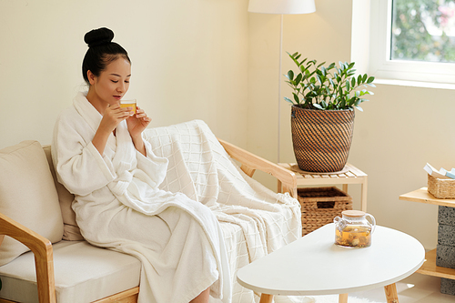 Portrait of positive young woman enjoying cup of chamomile tea to relax after taking bath