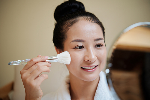 Smiling young woman applying liquid foundation with synthetic make-up brush