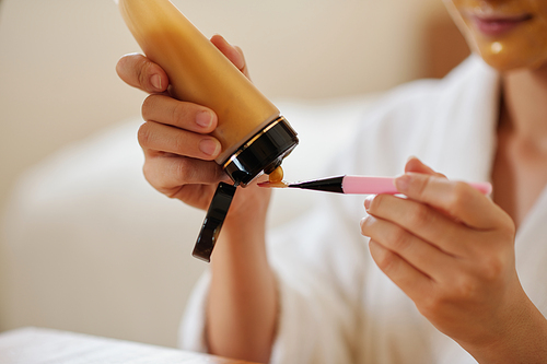 Closeup image of woman putting firming and brightening face mask on synthetic brush