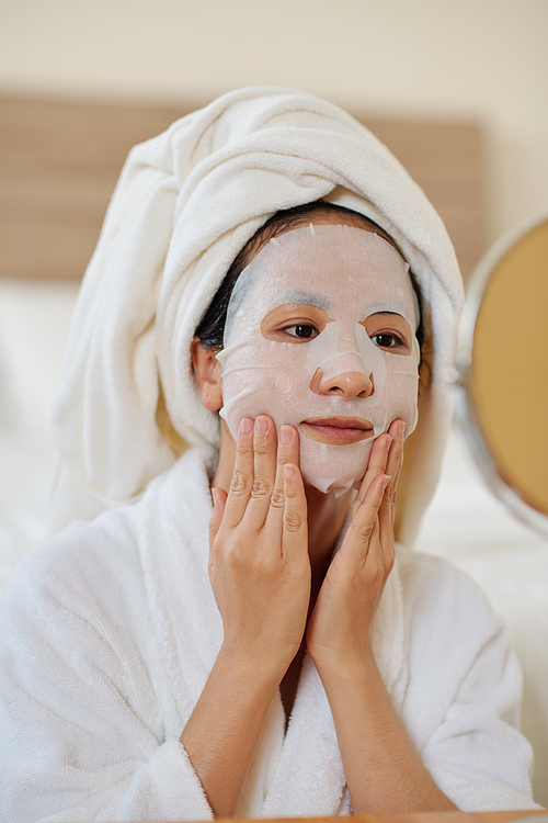 Young woman applying sheet face mask to moisturize skin after shower