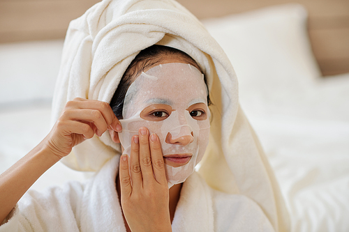Portrait of young woman applying face mask enriched with brightening serum