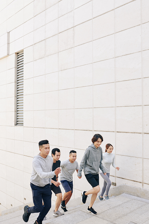 Group of fit young Asian people in sports clothes running up the stairs