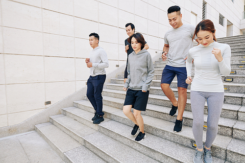 Fit young Asian men and women running down the stairs in city when training for marathon in the morning