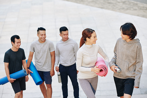 Cheerful young sporty Vietnamese people with yoga mats walking home after outdoor training