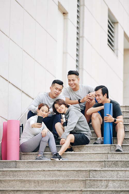 Group of cheerul young Asian people sitting on steps after training and taking selfie together