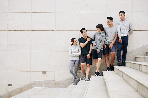 Group of smiling fit young people in sports clothes standing on steps after training and discussing upcoming marathon