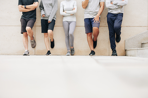 Cropped image of young people in sports clothes leaning on wall when standing on street after training