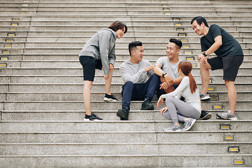 Group of happy excited young Vietnamese people sitting on steps and discussing training and joking around