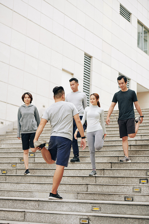 Group of fit young Asian people standing on steps and stretching hips after jogging outdoors