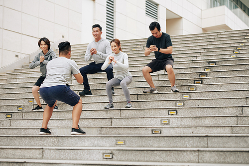 Young Asian people repeating after coach and doing squats to strengthen legs and core muscles