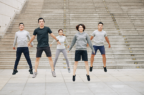 Group of fit young Asian people doing squat jumps outdoors when training for marathon together