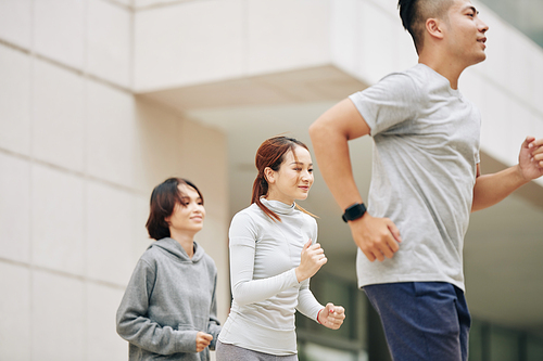 Pretty young Vietnamese woman running outdoors with group of friends to get ready for marathon