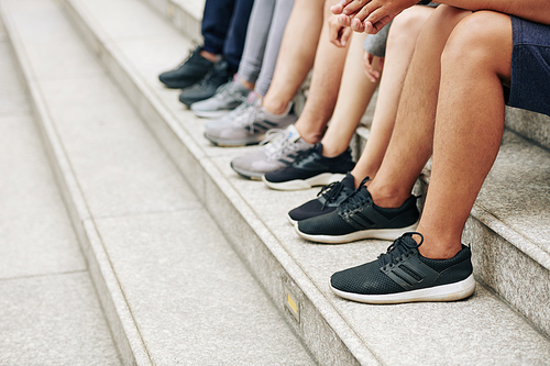 Cropped image of sports people in shorts and sneakers sitting on steps after outdoor training