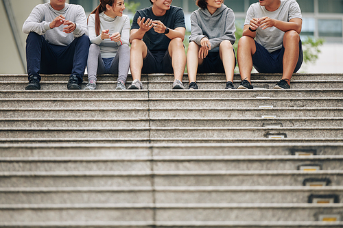 Cheerful positive young Asian people sitting outdoors after morning jog and discussing advantages of active lifestyle