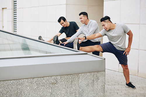 Young Vietnamese men stretching legs after jogging, trying to touch toes