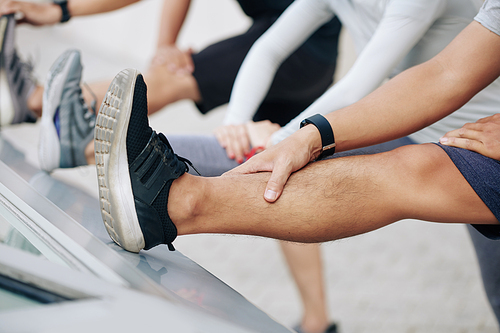 Close-up image of young men bending forward to straight lifted legs trying to touch toes