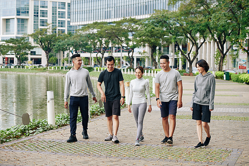 Positive young Vietnamese people walking in park around city pond after training outdoors together