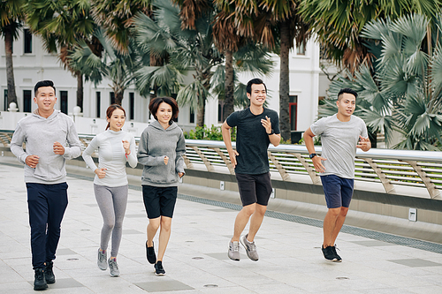 Group of young happy fit Asian friends jogging together in city park