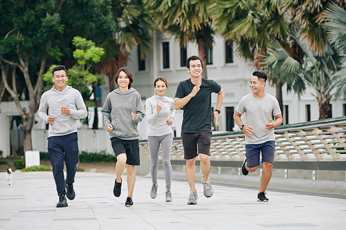 Cheerful young Vietnamese people enjoying running and training together in city park