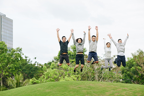 Excited happy young Vietnamese people jumping in city park after finishing outdoor training