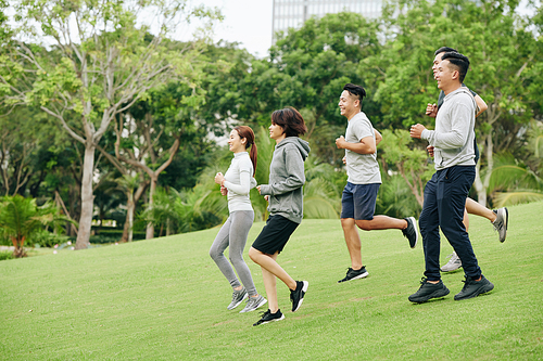 Group of positive young Vietnamese men and women jogging in city park together in the morning