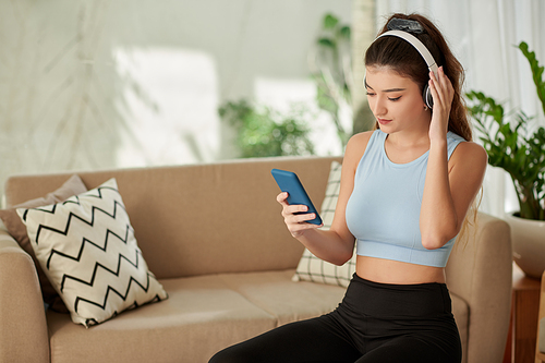 Fit young woman listening to music in headphones from playlist on smartphone