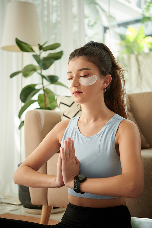 Young woman with under-eye patches meditaing at home in the morning