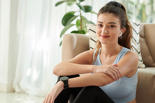 Portrait of smiling lovely young woman resting on floor after working out at home