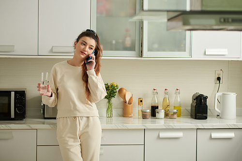 Young woman drinking water and talking on phone with friend
