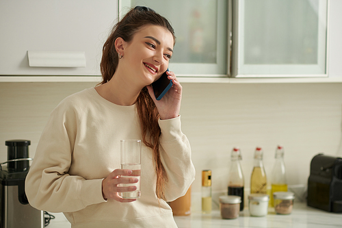 Portrait of young smiling woman drinking glass of fresh water and talking on phone