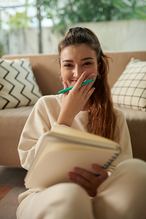 Portrait of joyful young woman drawing sketches or writing essay in textbook
