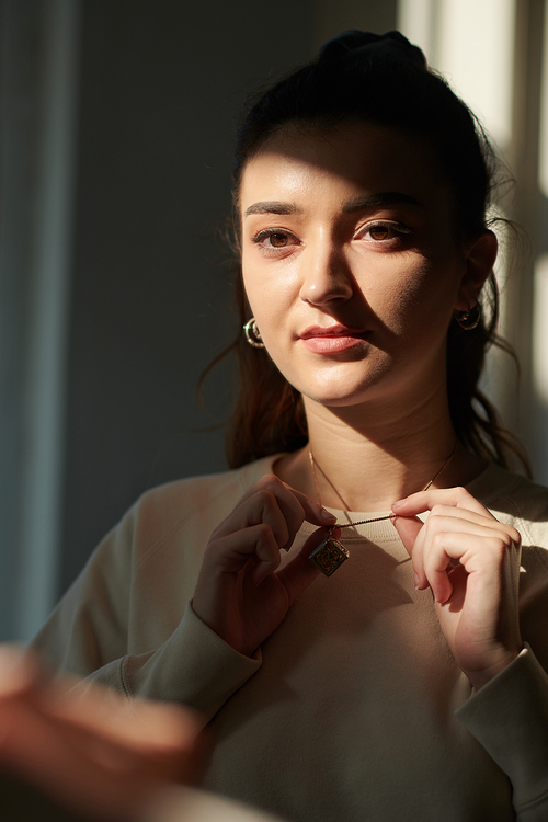 Portrait of serious young woman putting on jewelry