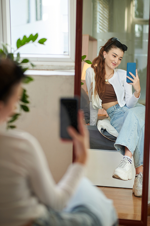 Smiling girl sitting in front of mirror and taking selfie