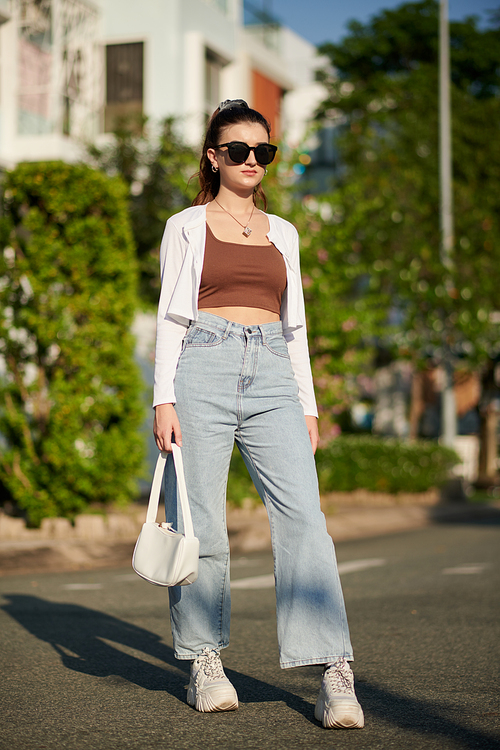 Young woman in wide jeans, sunglasses and white cardigan