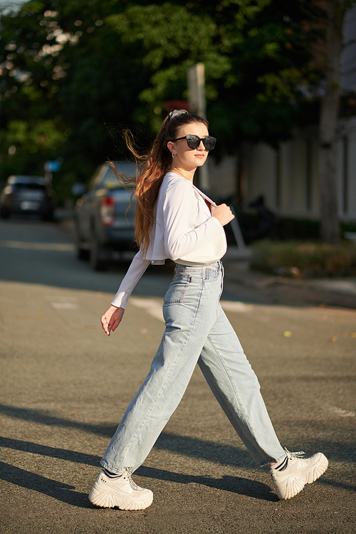 Young woman in sunglasses crossing road in city