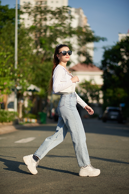 Young woman in sunglasses crossing road in city