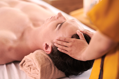 Masseuse giving relaxing head massage to young man