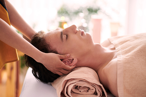 Young man getting relaxing head and neck massage in spa salon