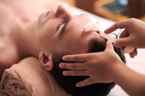 Closeup image of beautician massaging face of client with roller