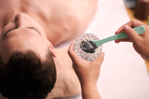 Beautician applying charcoal mask on face of male client